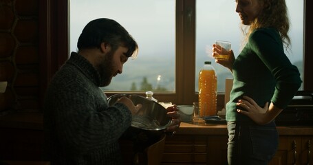 Adult man cook with wife in holiday house kitchen. Romantic couple talk and cook breakfast in wooden house. Travelers family stopped to rest in cottage during vacation trip. Concept of active leisure.