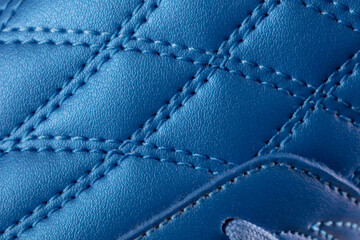 The macro texture of a blue leather sneaker with stitching. Part of the sports shoe is a close-up.