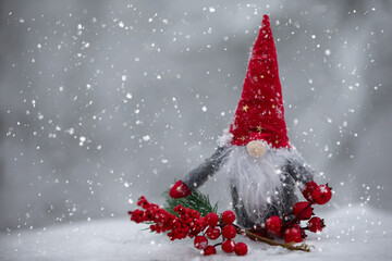 Naklejka na ściany i meble Christmas gnome with festive decorations on a background snow-covered fir branches. Christmas or New Year greeting card.