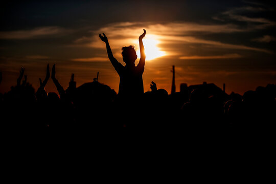 An unrecognizable group of people waves their hands at a concert or public event against the backdrop of the setting sun. Night music festival.