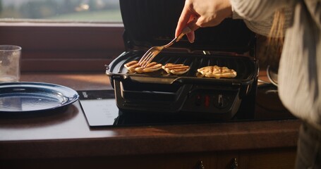 Close up shot of woman keeping bowl in hands and putting dough on grill using spoon. Two women together cook pancakes on breakfast. Family of tourists stopped in holiday house during vacation trip.