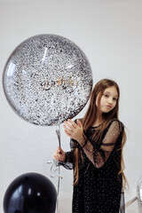 Naklejka premium A little girl celebrates her 10th birthday. A girl on a white background in a black dress with long straight hair. Party, holiday
