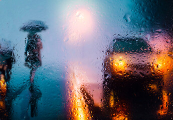 View through a glass window with raindrops on a blurred silhouette of a girl on a autumn city...