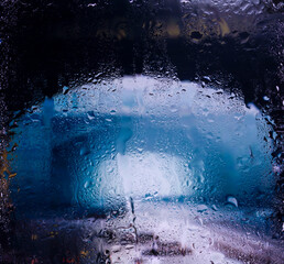 view through glass covered with raindrops onto the street of a small European town covered in morning fog. focus on raindrops	