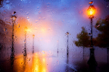 View through a glass window with raindrops on a broken silhouette of a girl with an umbrella...