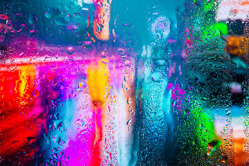 View through a glass window with raindrops on city streets with cars in the rain, bokeh of colorful city lights, night street scene. Focus on raindrops on glass	