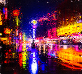 View through a glass window with raindrops on city streets with cars in the rain, bokeh of colorful city lights, night street scene. Focus on raindrops on glass	
