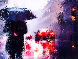 View through a glass window with raindrops on a broken silhouette of a girl with an umbrella...