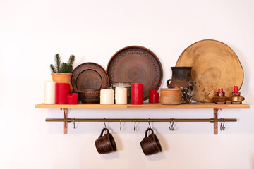 Cups hanging on metal cuisine railing on wall. Wooden shelf with various clay cookware and...
