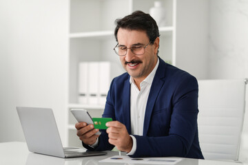 Confident businessman in glasses and a blue suit holds a green credit card