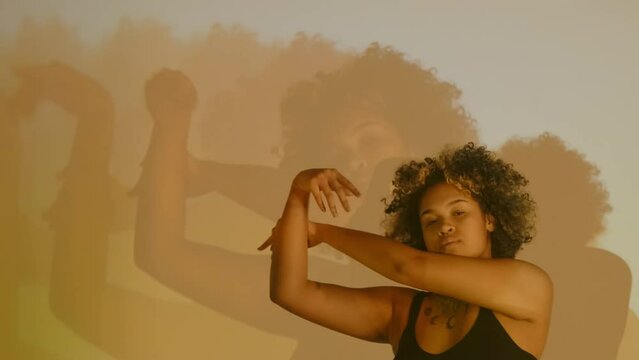 Horizontal slow motion studio shot of young African American woman dancing in projector light with her image repeating on background