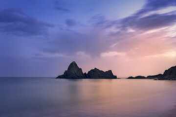 Sunrise on Saturraran beach with rocks and water in the foreground and a rock formation in the...