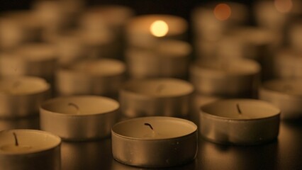 Rows of candles. A single candle burns among the many dotted around. The concept of a memorial day....