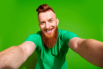 Photo of optimistic funky man with ginger beard dressed green t-shirt making selfie on smartphone...
