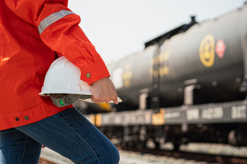 Close-up at a worker is holding white safety helmet, posing on crude oil tanker freight train as...