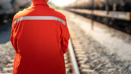 Close-up at back of a worker in safety uniform suit with reflection sight bar, standing on the train locomotive and railway track as background. Ready to working in transportation industrial concept. - obrazy, fototapety, plakaty