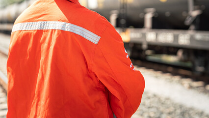 Close-up at back of a worker in safety uniform suit with reflection sight bar, standing on the train locomotive and railway track as background. Ready to working in transportation industrial concept.