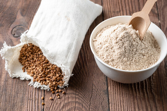 Buckwheat in a canvas bag and buckwheat flour in a bowl on a wooden table. Gluten free buckwheat flour.