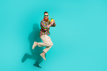 Fototapeta na wymiar Full body size photo of carefree red hair hipster guy jumping and enjoying fresh juice pineapple isolated on aquamarine color background