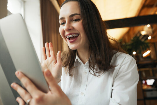 Close up photo of young woman with dental braces smiling while chatting online in tablet sitting at comfortable office. Selective focus. Concept of medicine and beauty, health care and confidence.
