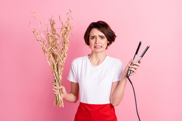 Photo portrait of worried hairdresser keeping hot hair straightener dry bunch isolated pastel pink...