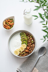 Granola with banana and kiwi on a white table with a green branch.