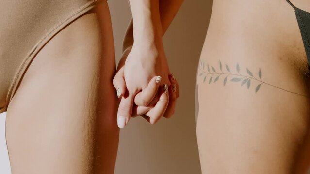 Close-up studio shot footage of unrecognizable young women in underwear standing in daylight holding hands