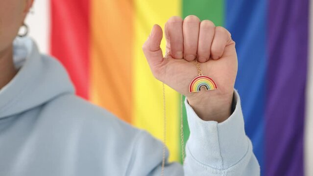 A focused close-up captures the essence of LGBT pride as a lesbian rights activist's hand carefully holds a rainbow-colored pendant, set against the backdrop of a pride flag. High quality 4k footage