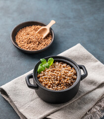 Buckwheat porridge with fresh herbs in a black pan on a napkin on a dark  background with raw grains.