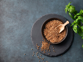 Raw buckwheat grains in a wooden bowl on a board on a dark background with fresh herb.