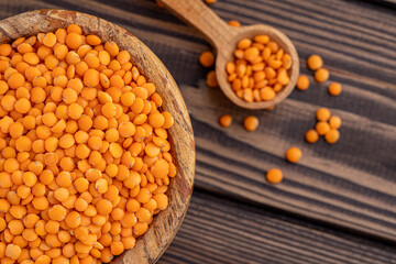 Photo of red lentils in wooden bowl with wooden measuring cup on wooden background.  Healthy lifestyle. Vegetarian and vegan diet.