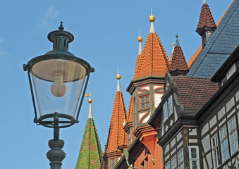 Roof towers and part of the half-timbered front gable of the Old Town Hall in Fulda, Germany, with street lamp and blue sky on a summer afternoon