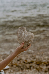 hand holding a heart shaped stone on the beach