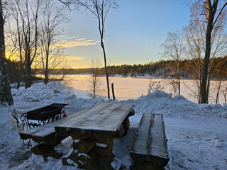 Wooden picnic table in winter, sunrise on the lake, winter landscape