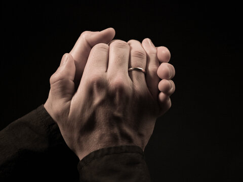 Hands intertwined within each other with black background.