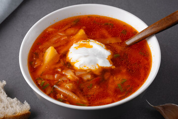 Close up borscht with sour cream in a bowl with bread on a gray table