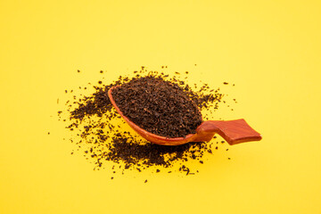 black tea in wooden spoon on yellow background. dry black tea on yellow background and in wooden...