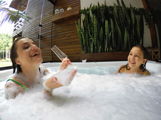 mãe e filha juntas felizes brincando em banheira de espumas em spa de luxo 