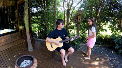 pai tocando violão para filha em casa de férias