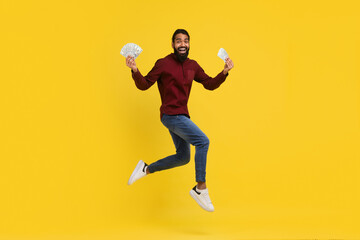 Fototapeta na wymiar Excited millennial indian guy holding money cash in hands, jumping