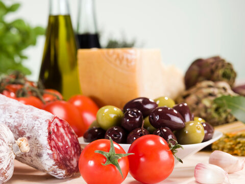 Still life of Italien food ingredients, olives, tomatoes, salami, parmesan, oil, artichokes.
