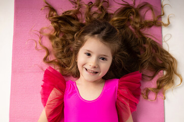 Tired little girl lying down after gym training on a yoga mat with long blonde hair scattered.