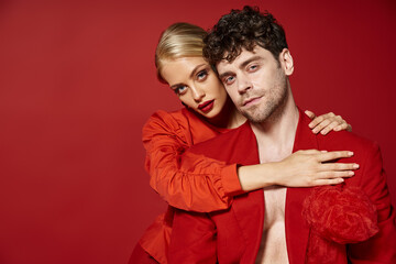 beautiful young woman with red lips and blonde hair embracing handsome man in red attire, fashion