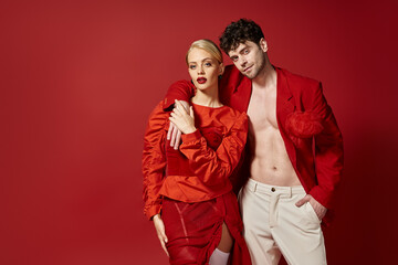 stylish man in red blazer and white pants posing while putting hand around neck of blonde woman