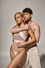 shirtless man with muscular body embracing pretty young woman on grey background, sexy couple