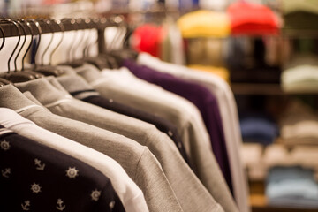 Knitted clothes, a row of T-shirts in light colors on hangers in a clothing store close-up, soft selective focus.