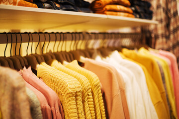 Colorful outerwear, a row of sweaters and knitted sweaters in yellow tones on hangers in a clothing...
