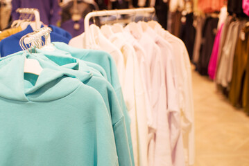 Colorful outerwear, row of blue hooded sweatshirts on hangers in a clothing store close-up, soft selective focus.