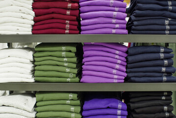 Pile of different colors of t-shirts with size sticker on shelves in a store 