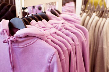 Colorful outerwear, a row of pink hooded sweatshirts on hangers in a clothing store close-up, soft selective focus.